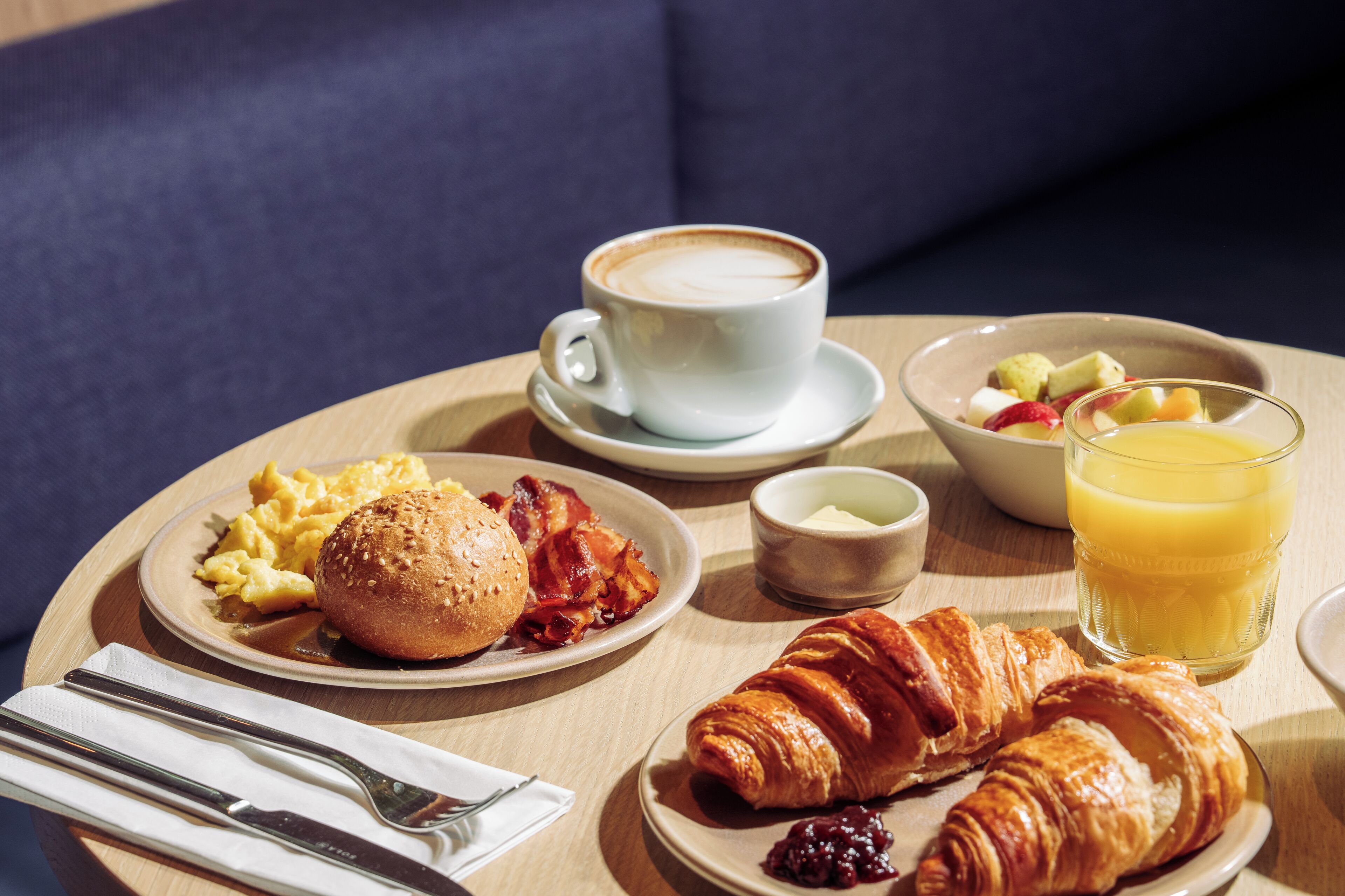 Breakfast items on a table including eggs, bacon, croissants, coffee, and fruit.