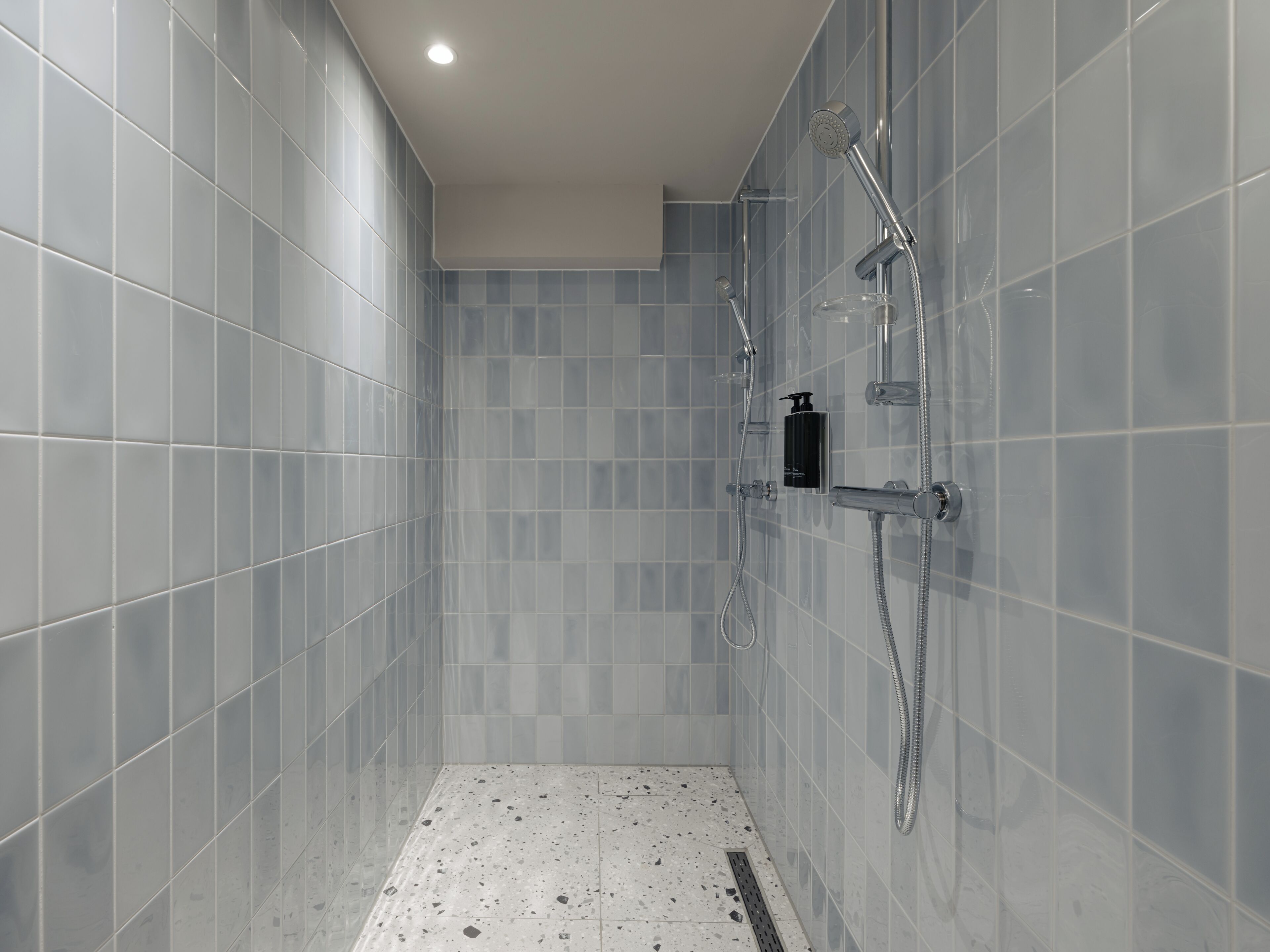 A modern shower with a handheld showerhead, a wall-mounted faucet, and a soap dispenser.