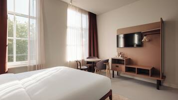 A hotel room with a large bed, a desk, a chair, a television, and a wardrobe.