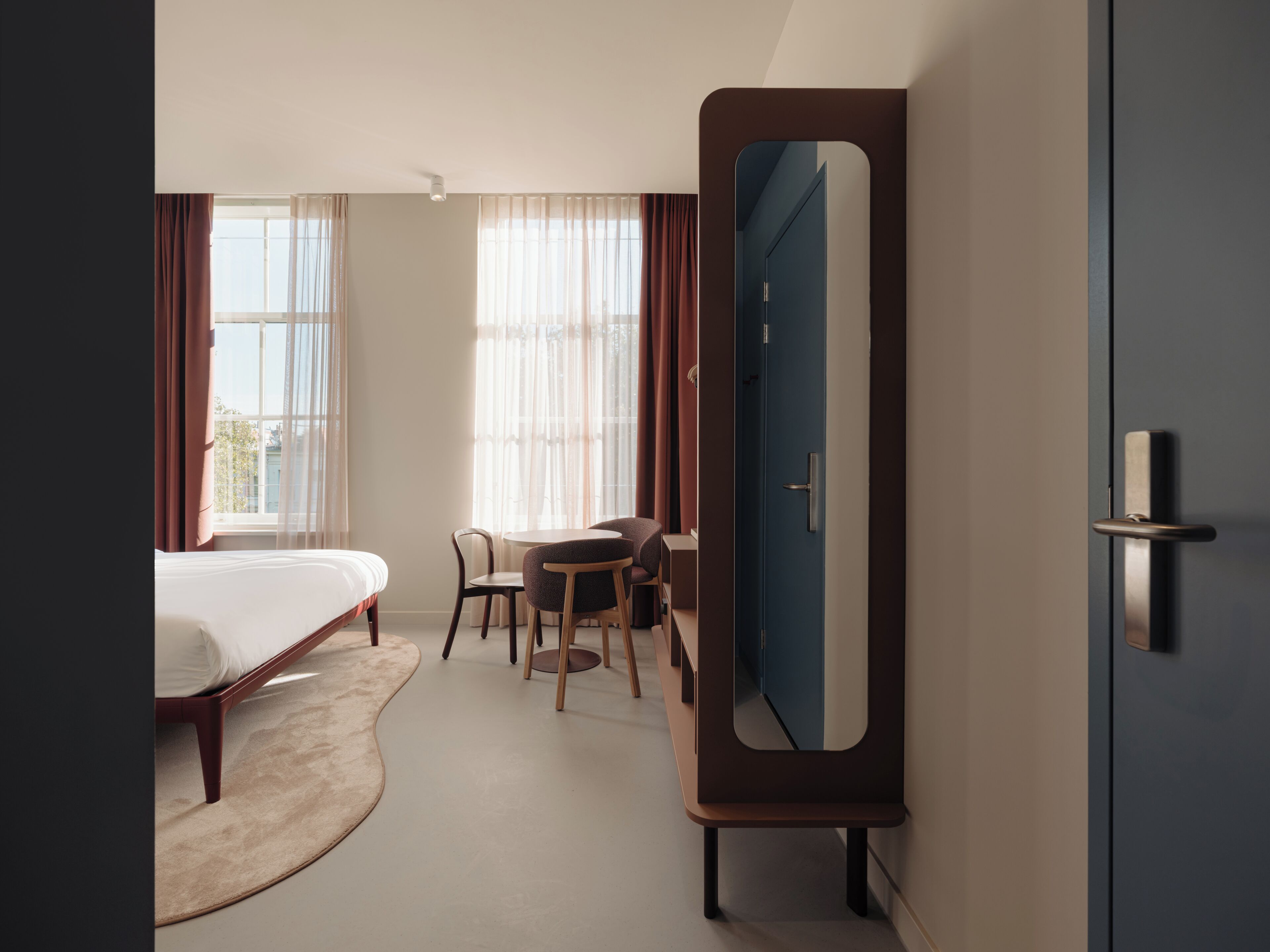 Ein Hotelzimmer mit Bett, Schreibtisch, Stuhl, Spiegel und Tür.