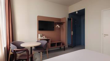 A hotel room with a bed, a desk with a chair, a TV mounted on the wall, and a wardrobe.