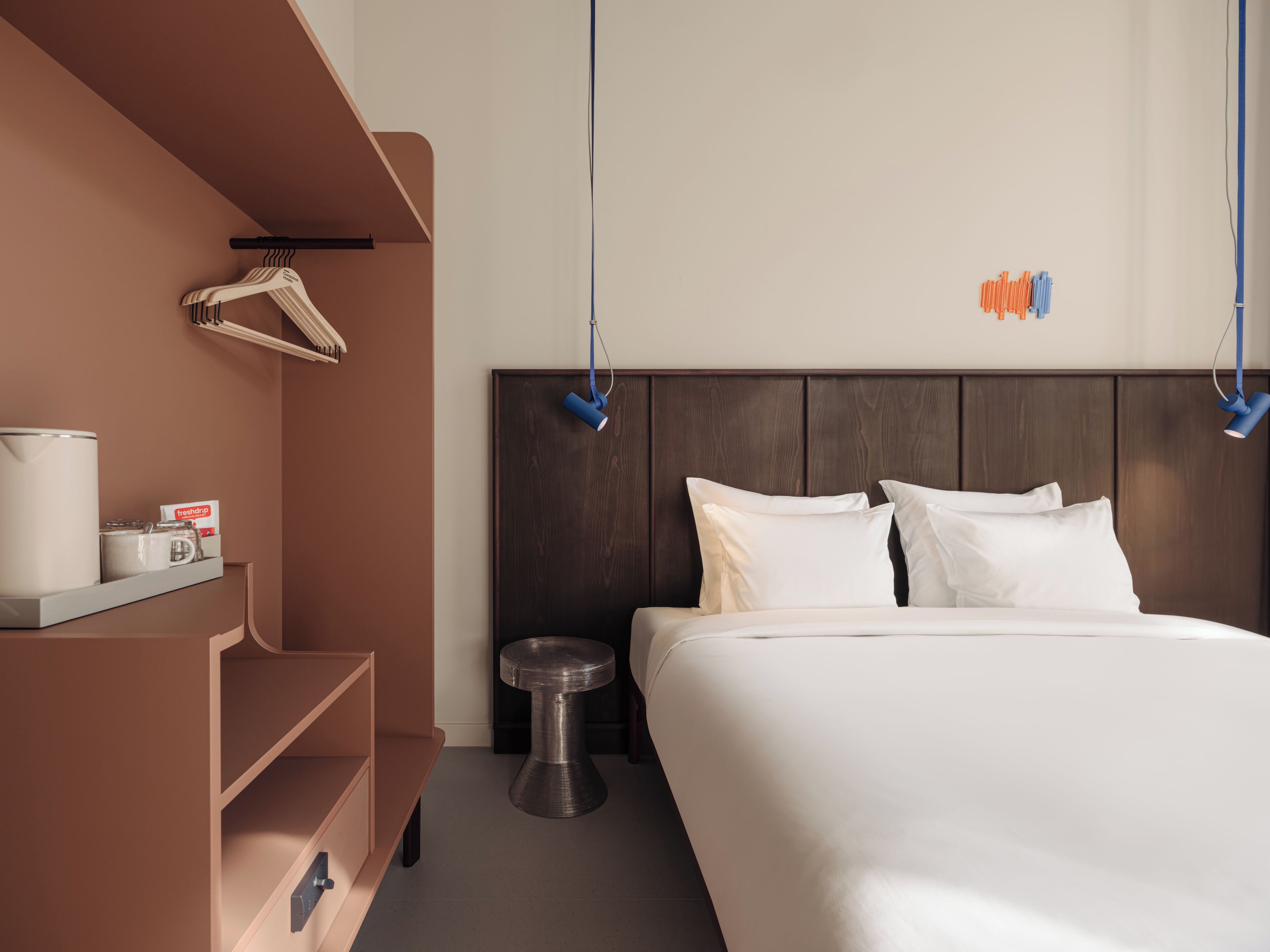 A modern hotel room with a large bed, a wooden wardrobe, a small round table, and a hanging light fixture.