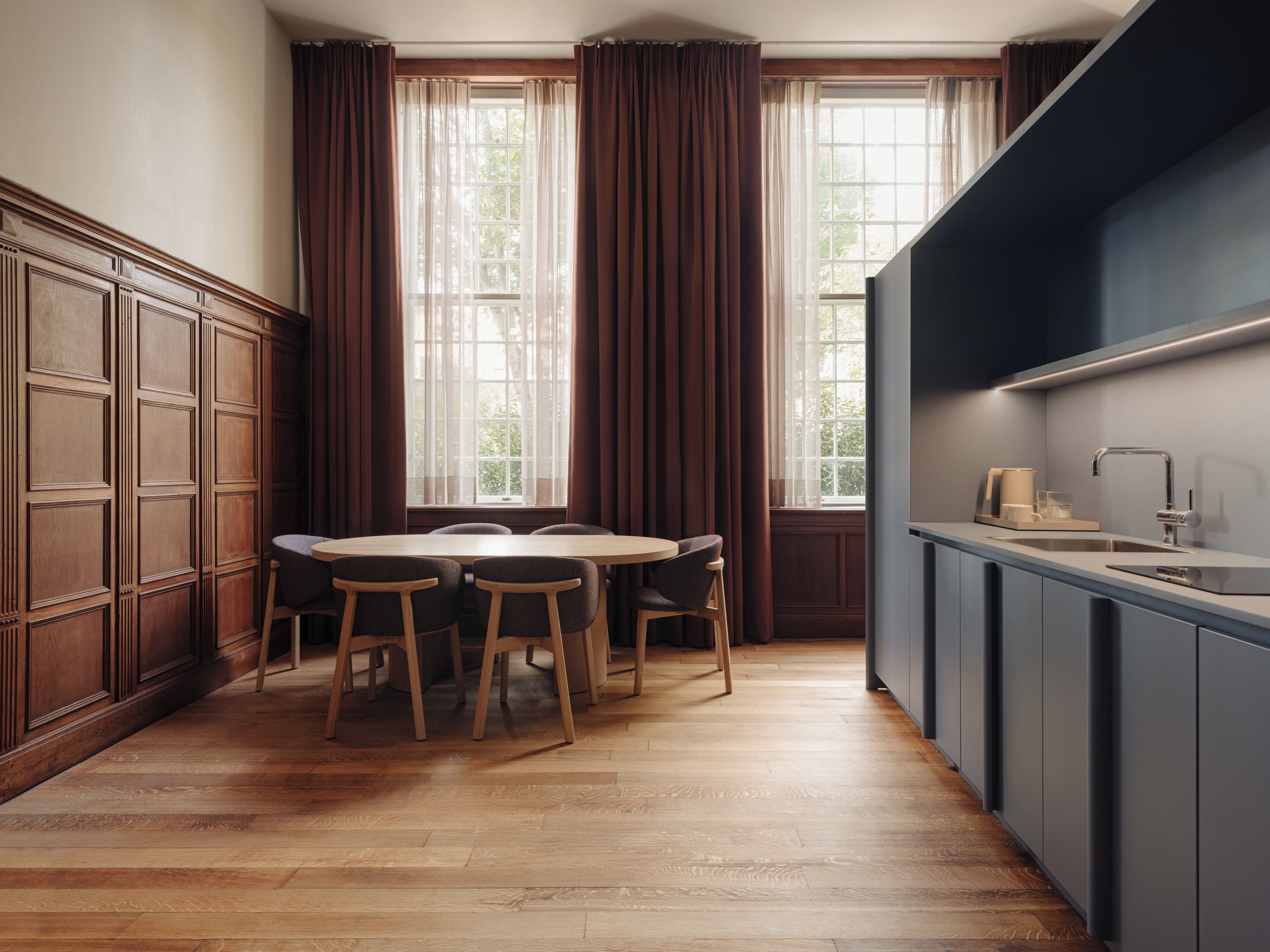 Una cocina moderna con armarios de madera, una mesa de comedor con sillas y un amplio ventanal con cortinas.