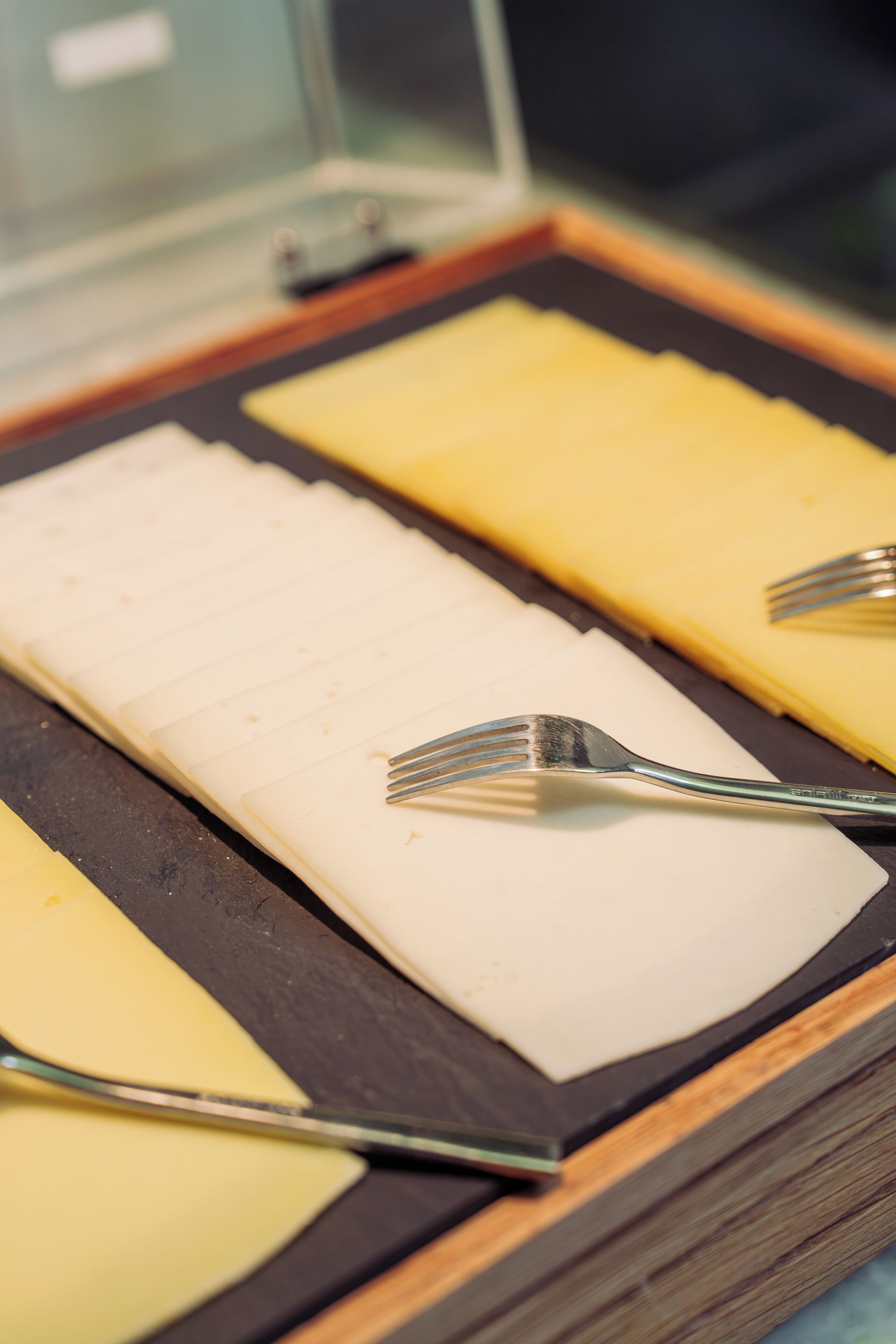 A tray with sliced cheese and two forks.