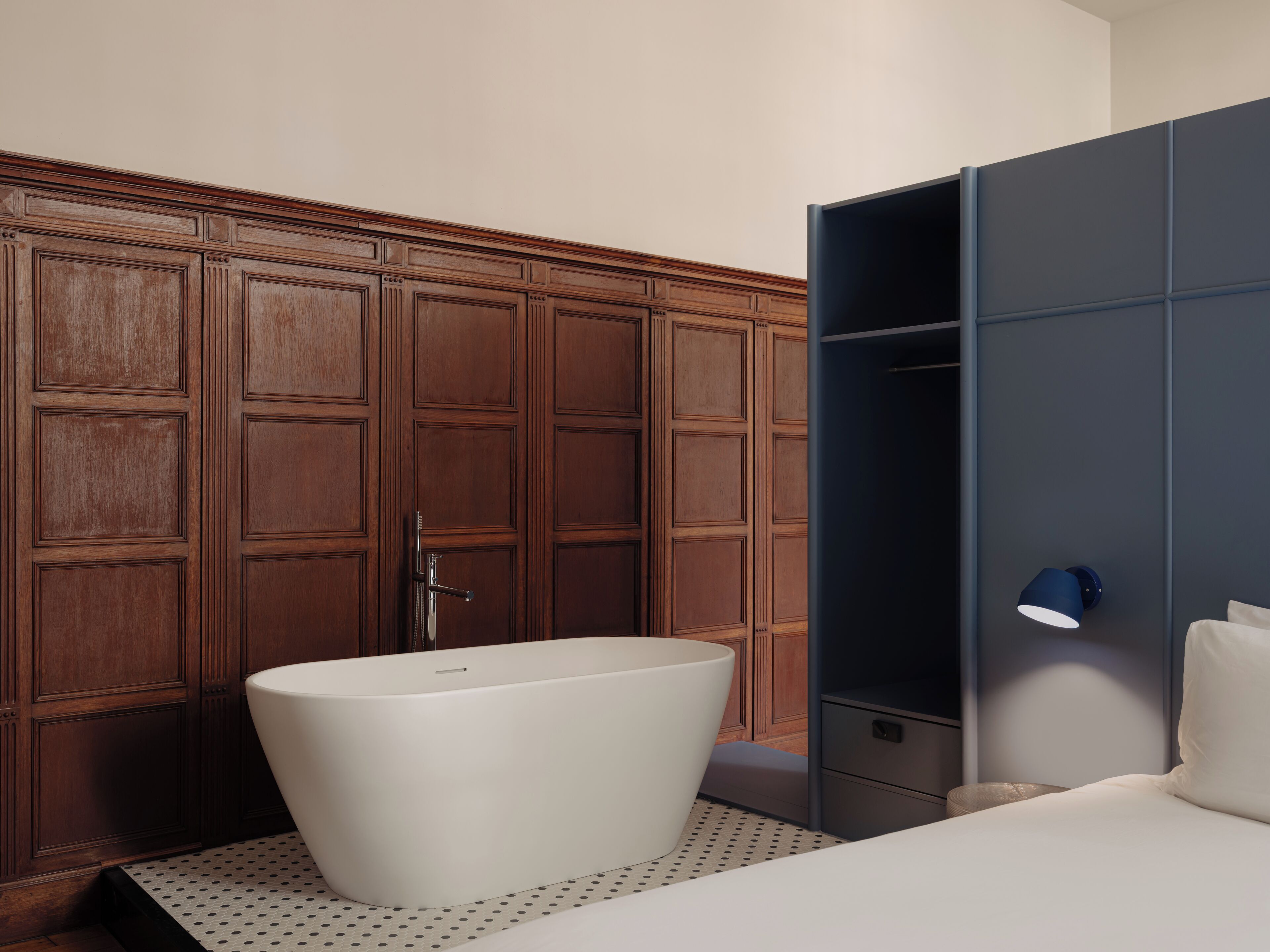 A modern bathroom with a freestanding bathtub, wooden paneling, and a dark blue wardrobe with a light fixture.