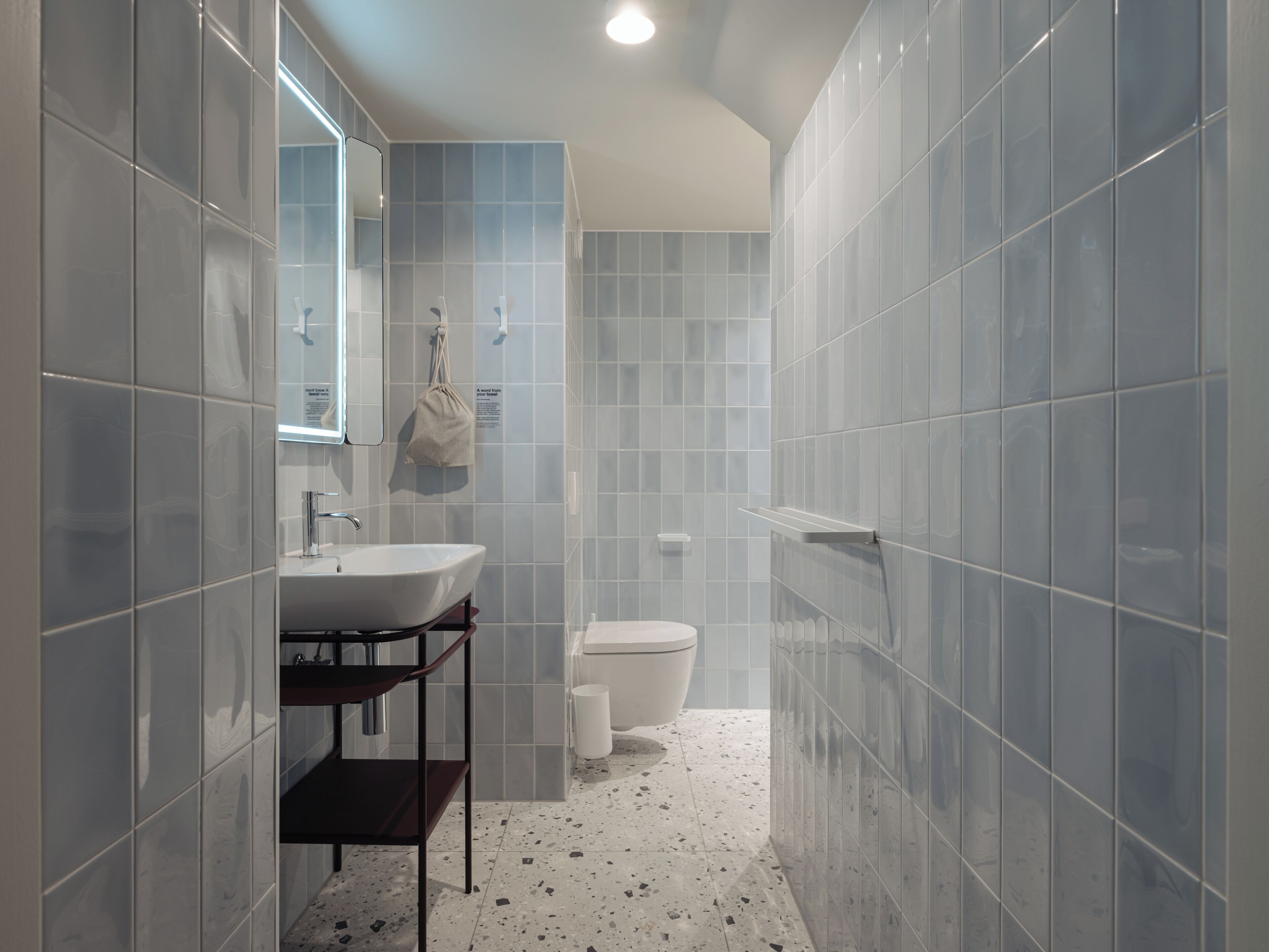 Un baño con lavamanos blanco, espejo y toallero.