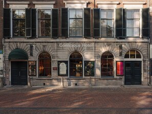 Ein historisches Gebäude mit zahlreichen Fenstern und Eingängen, mit der Aufschrift 'Conscious Hotel'.