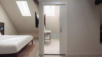 A bedroom with a bed, a desk, a chair, a window, and a door leading to a bathroom.