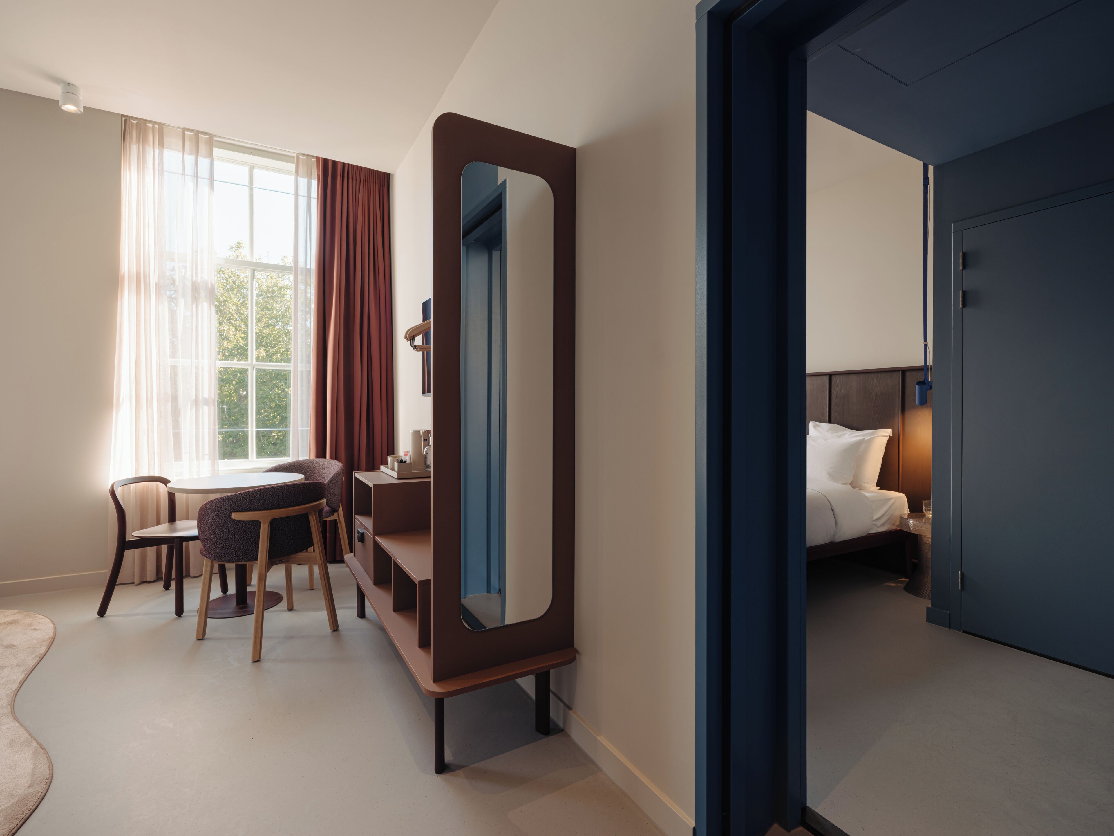 Une chambre d’hôtel équipée d’un lit, d’un bureau, d’une chaise, d’un miroir et offrant une vue sur l’extérieur.