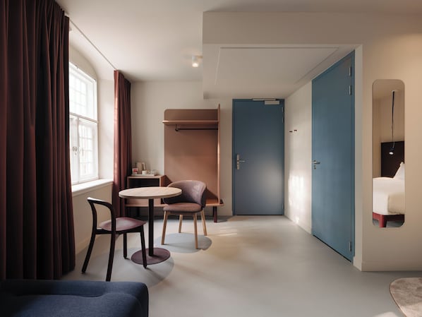 Una habitación de hotel moderna con una mesa redonda, dos sillas, un sofá, un armario y una pequeña zona de kitchenette.