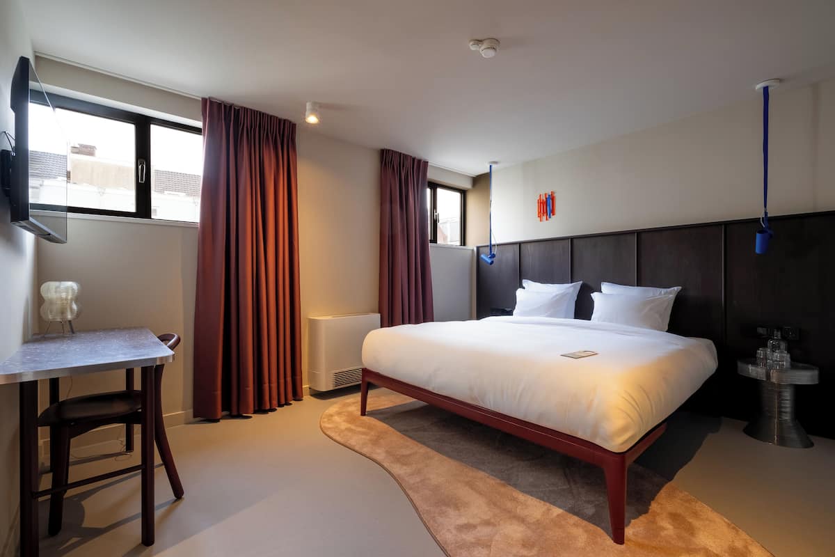 A modern hotel room with a large bed, a desk, and a TV.