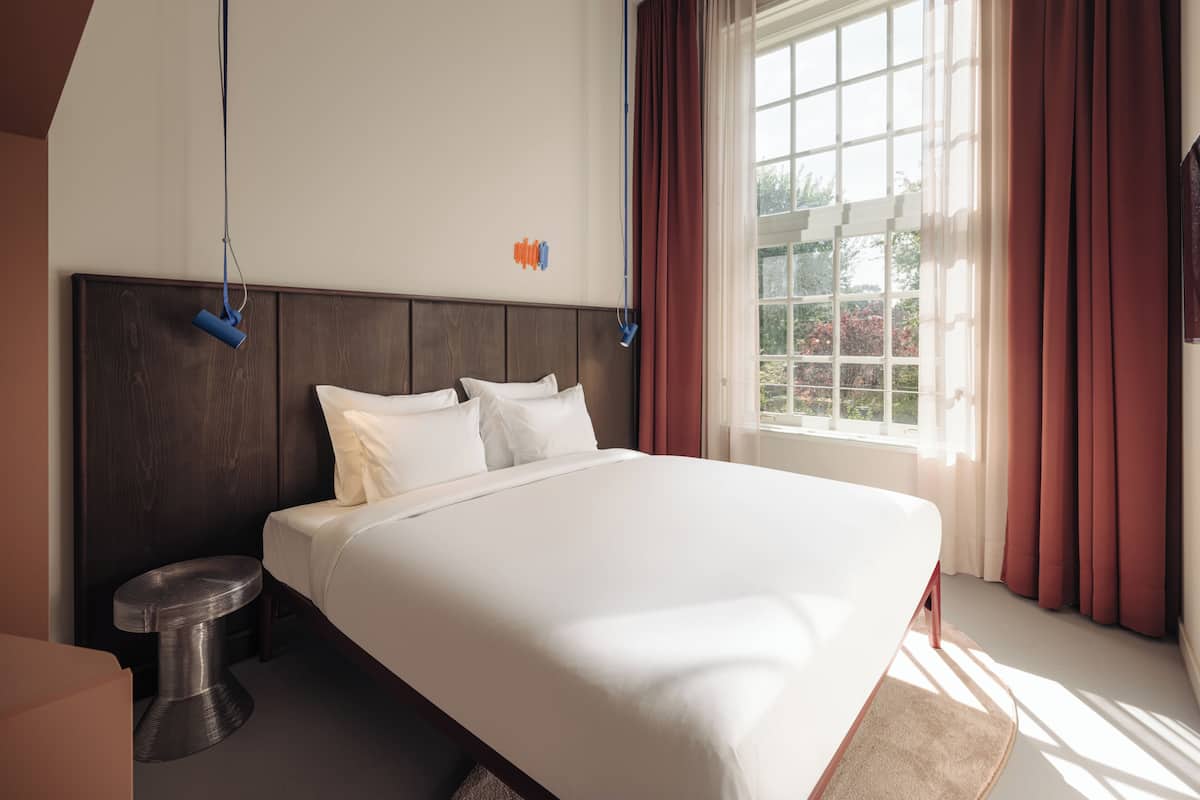 A hotel room with a large bed, a wooden headboard, a small round table, and a window with curtains.