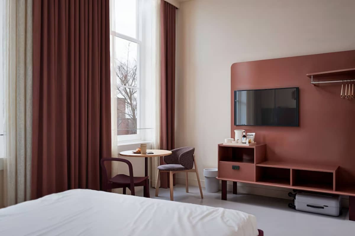 Ein Hotelzimmer mit Bett, Schreibtisch, Stuhl, Fernseher und Minibar.