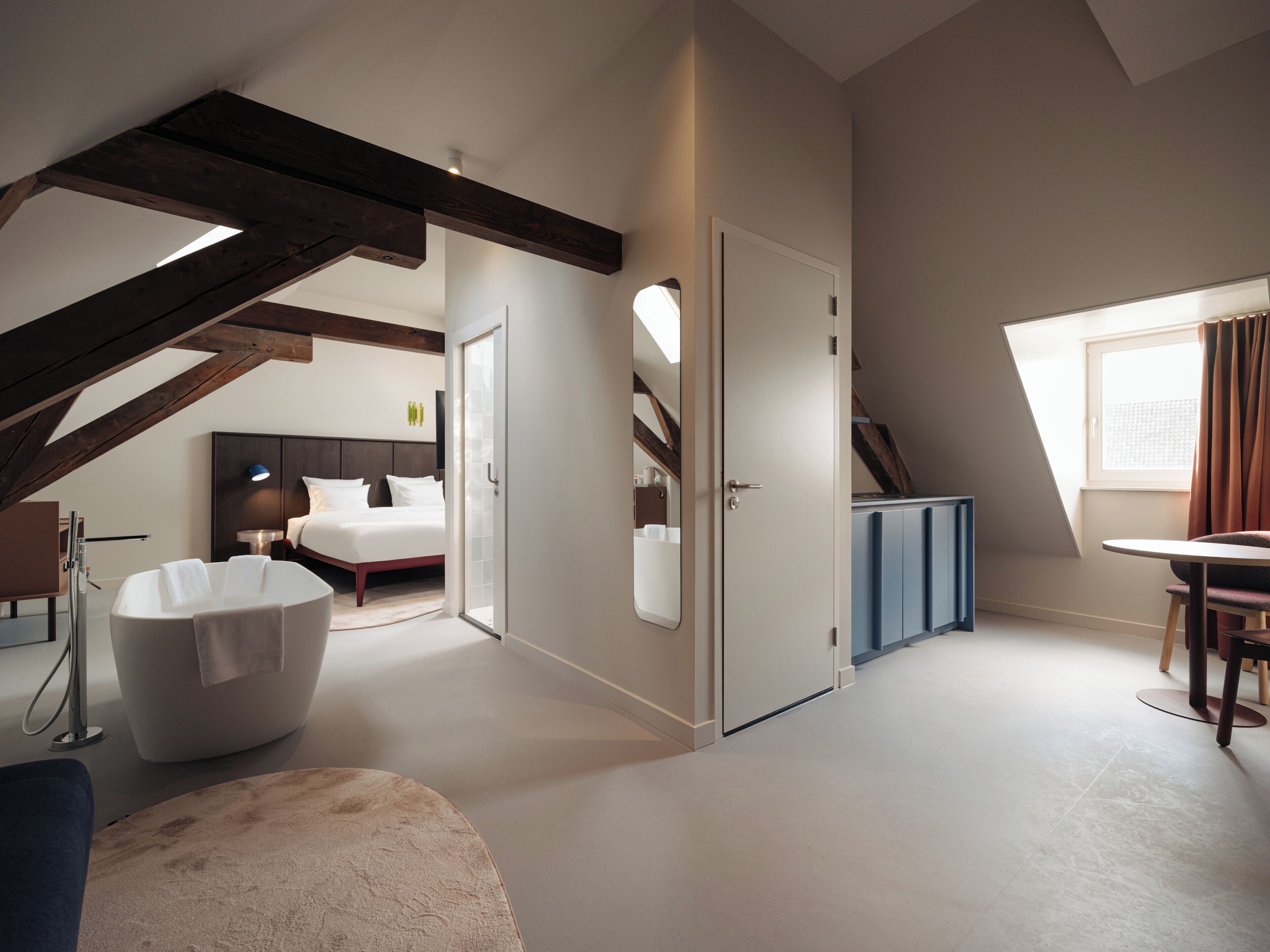 A modern bedroom with a large bed, a white bathtub, and a dining area with a table and chairs.