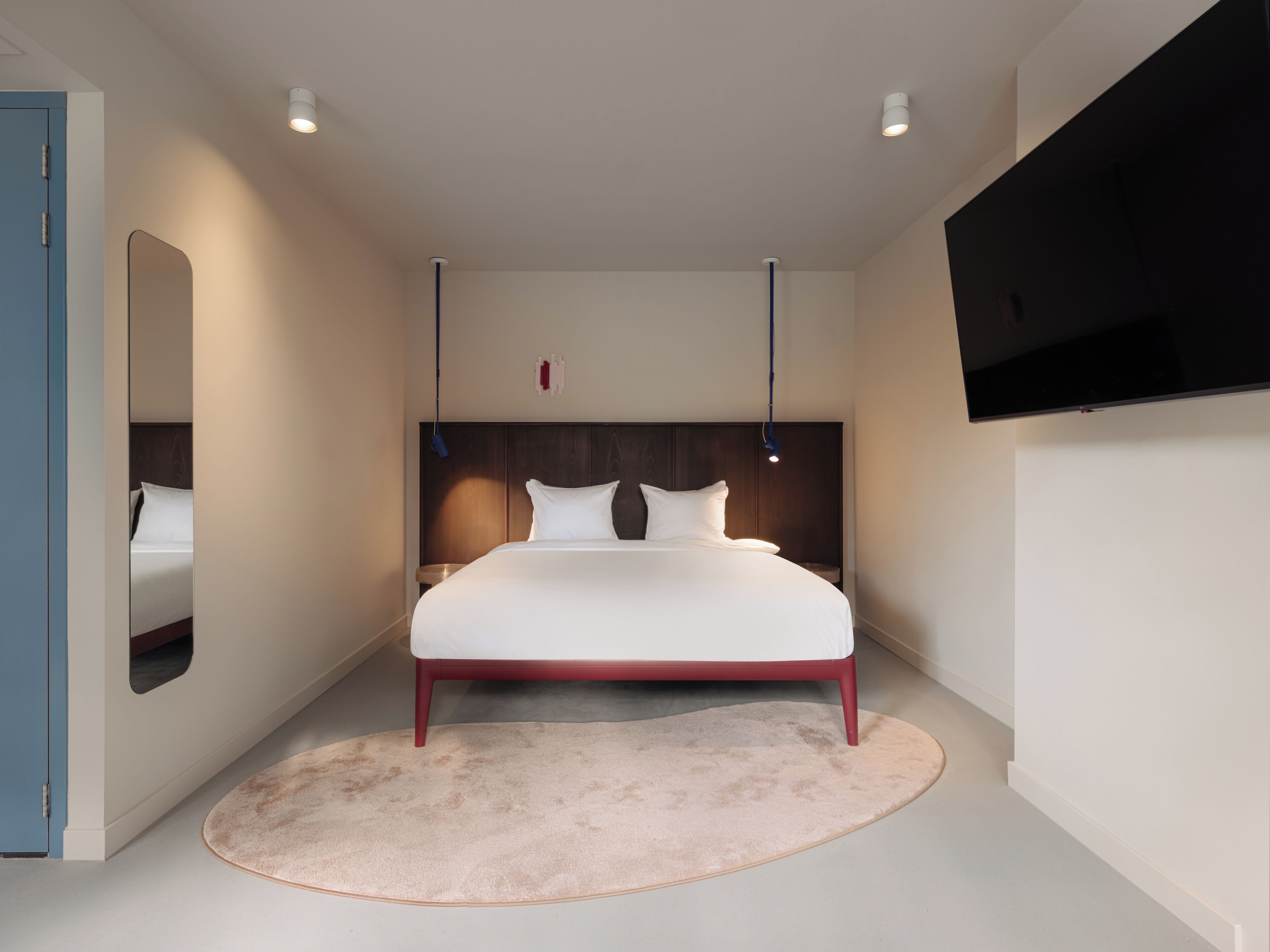 Une chambre à coucher moderne avec un grand lit, un téléviseur à écran plat fixé au mur et un tapis rond.