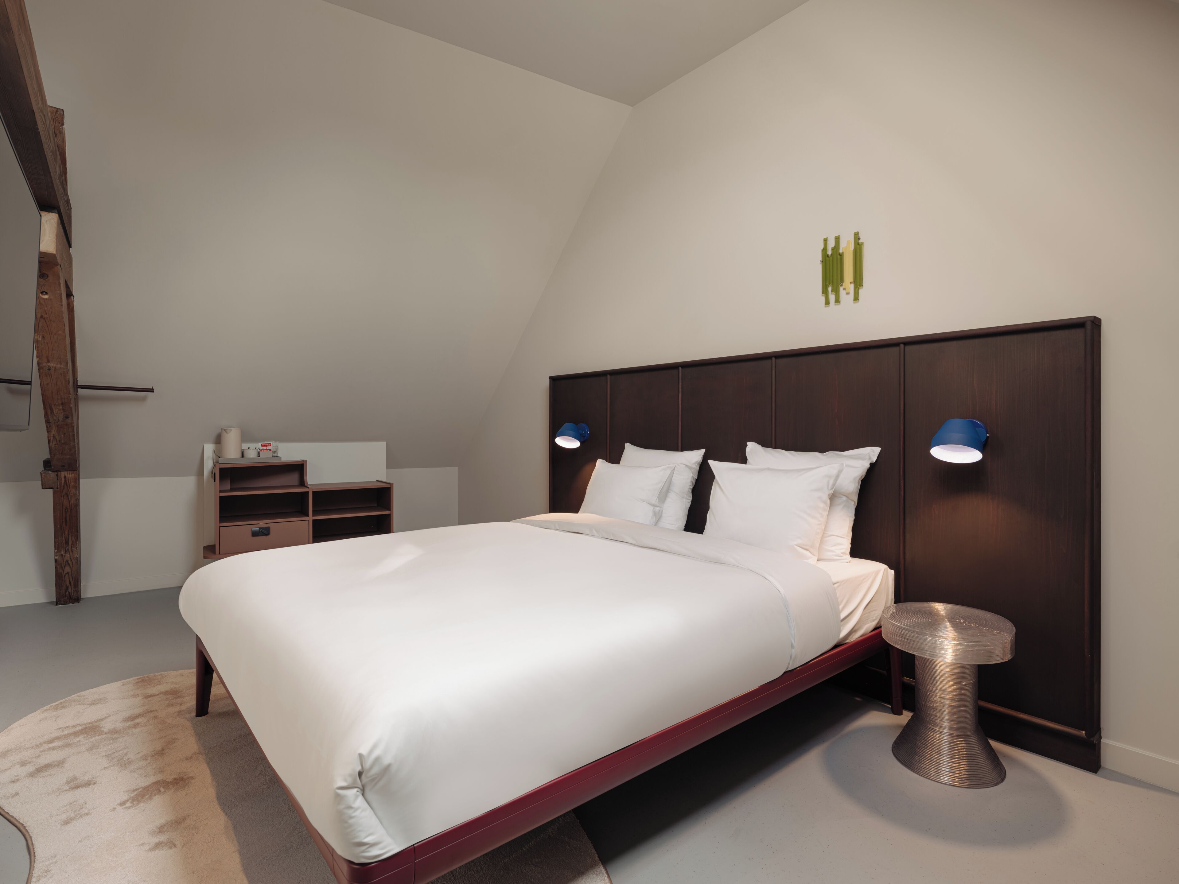 A modern bedroom with a large bed, two bedside lamps, a wooden headboard, and a small round table.
