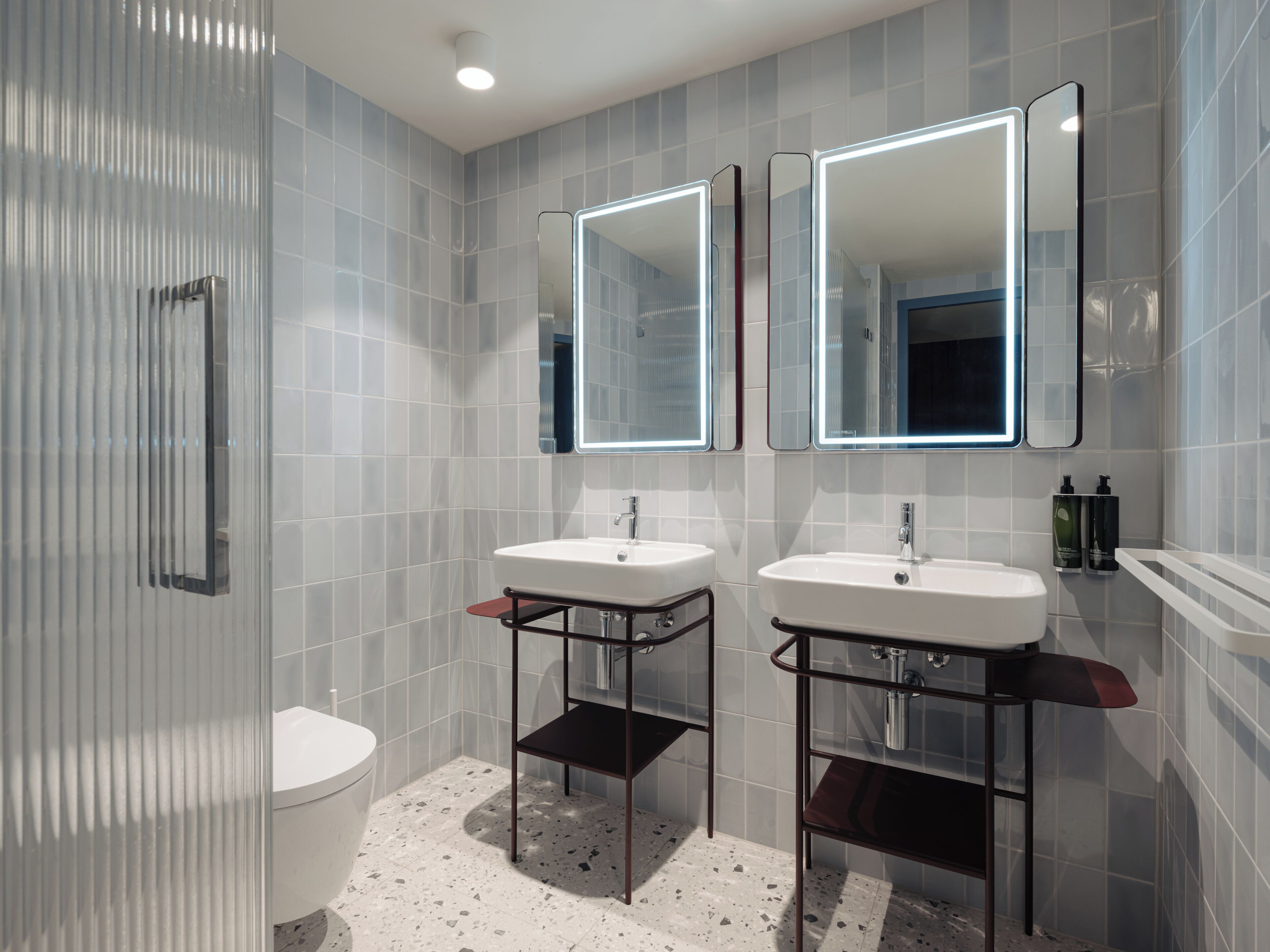 A modern bathroom with two sinks, a toilet, and a shower area.