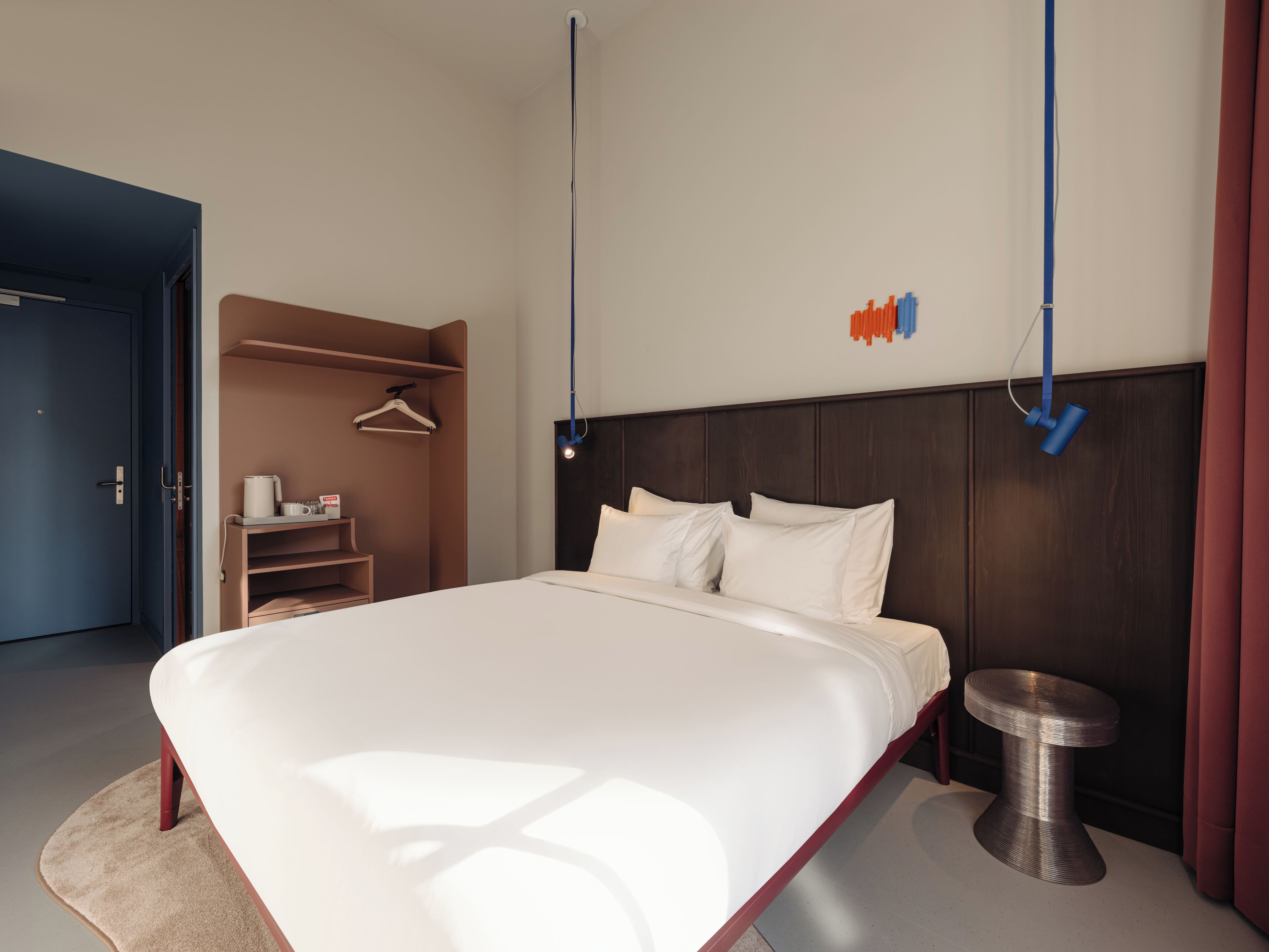 Une chambre d’hôtel moderne avec un grand lit, une table de chevet, une armoire et un luminaire suspendu.