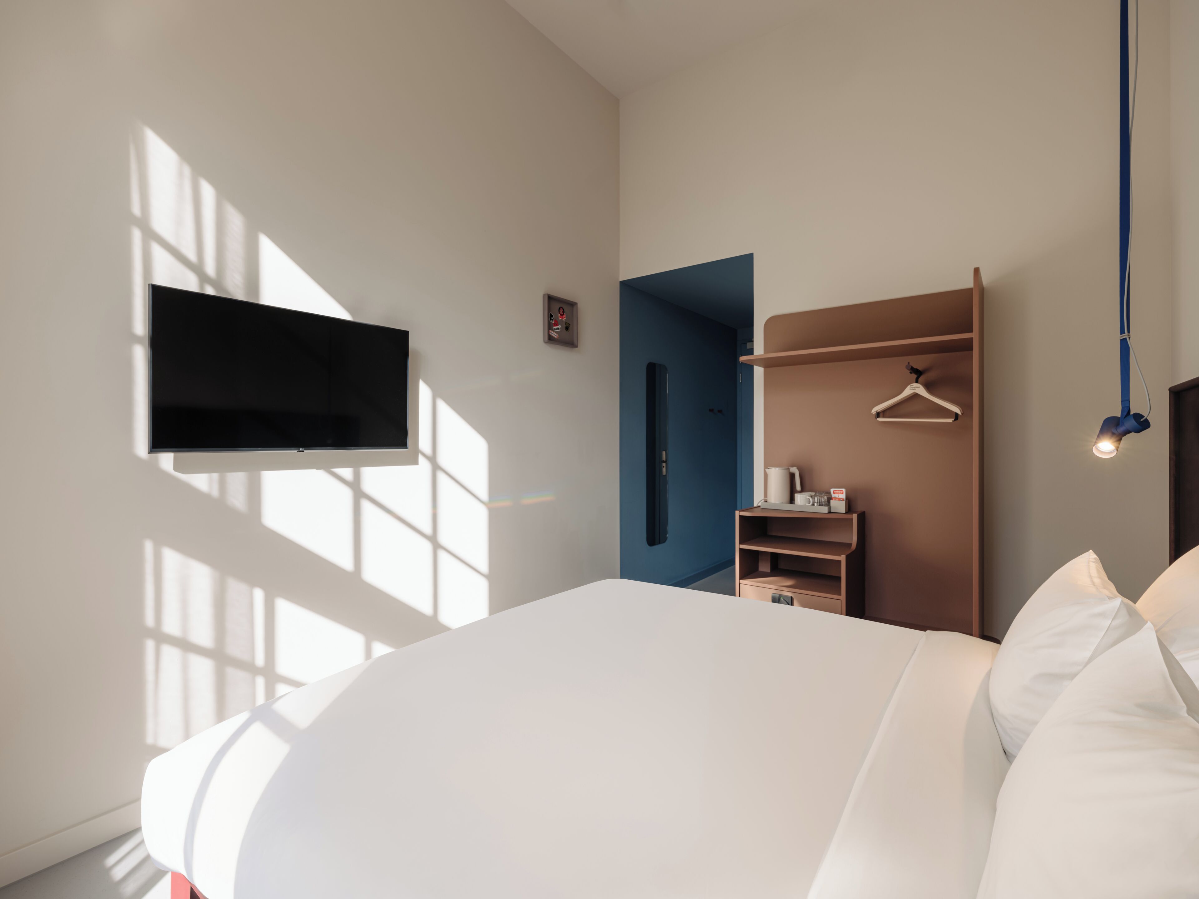 A modern bedroom with a bed, a TV mounted on the wall, a wardrobe, and a door leading to another room.