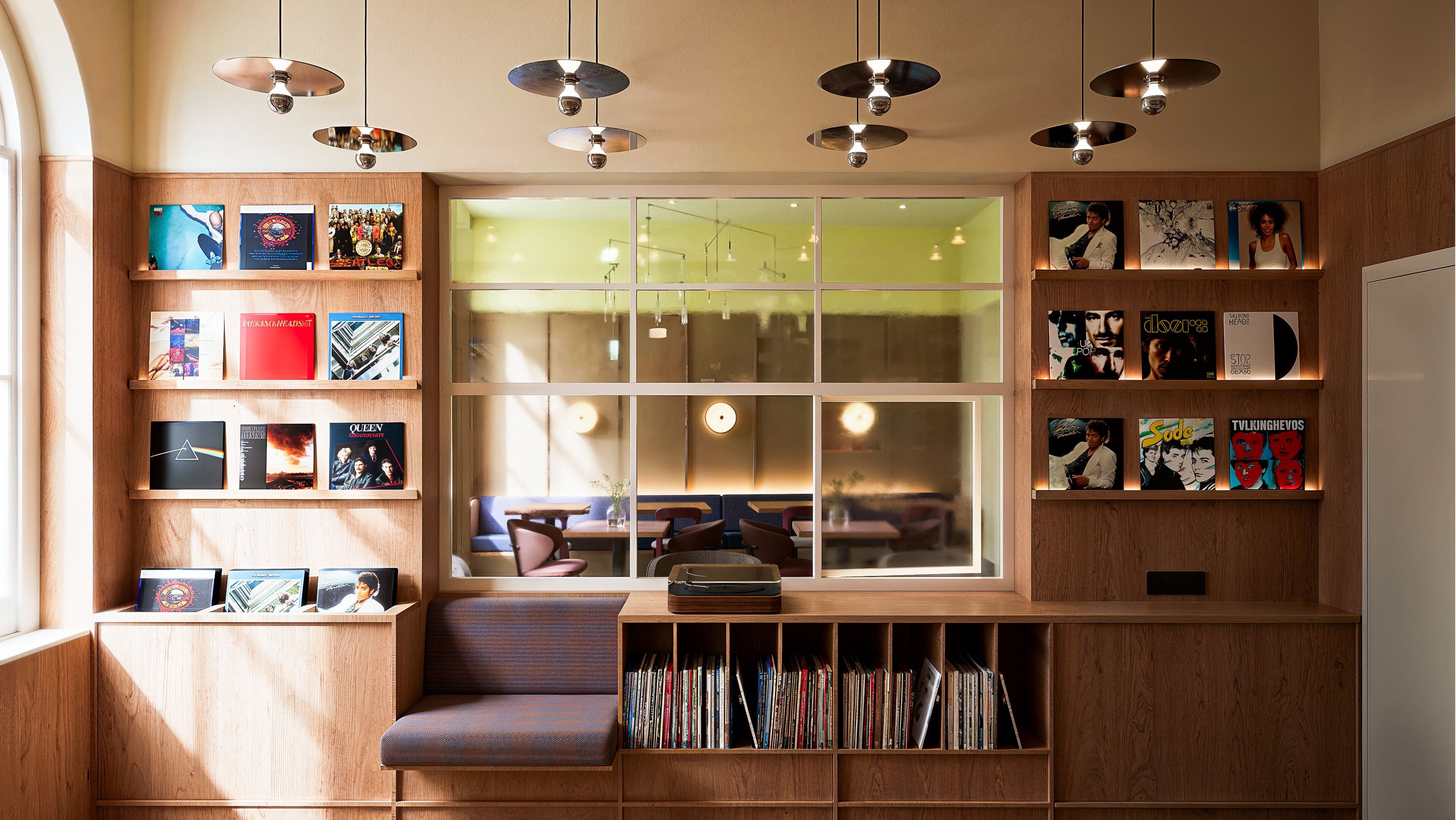 Un rincón acogedor para leer con estanterías de madera que muestran libros y cuadros enmarcados, un sillón cómodo y un ventanal con luz natural.