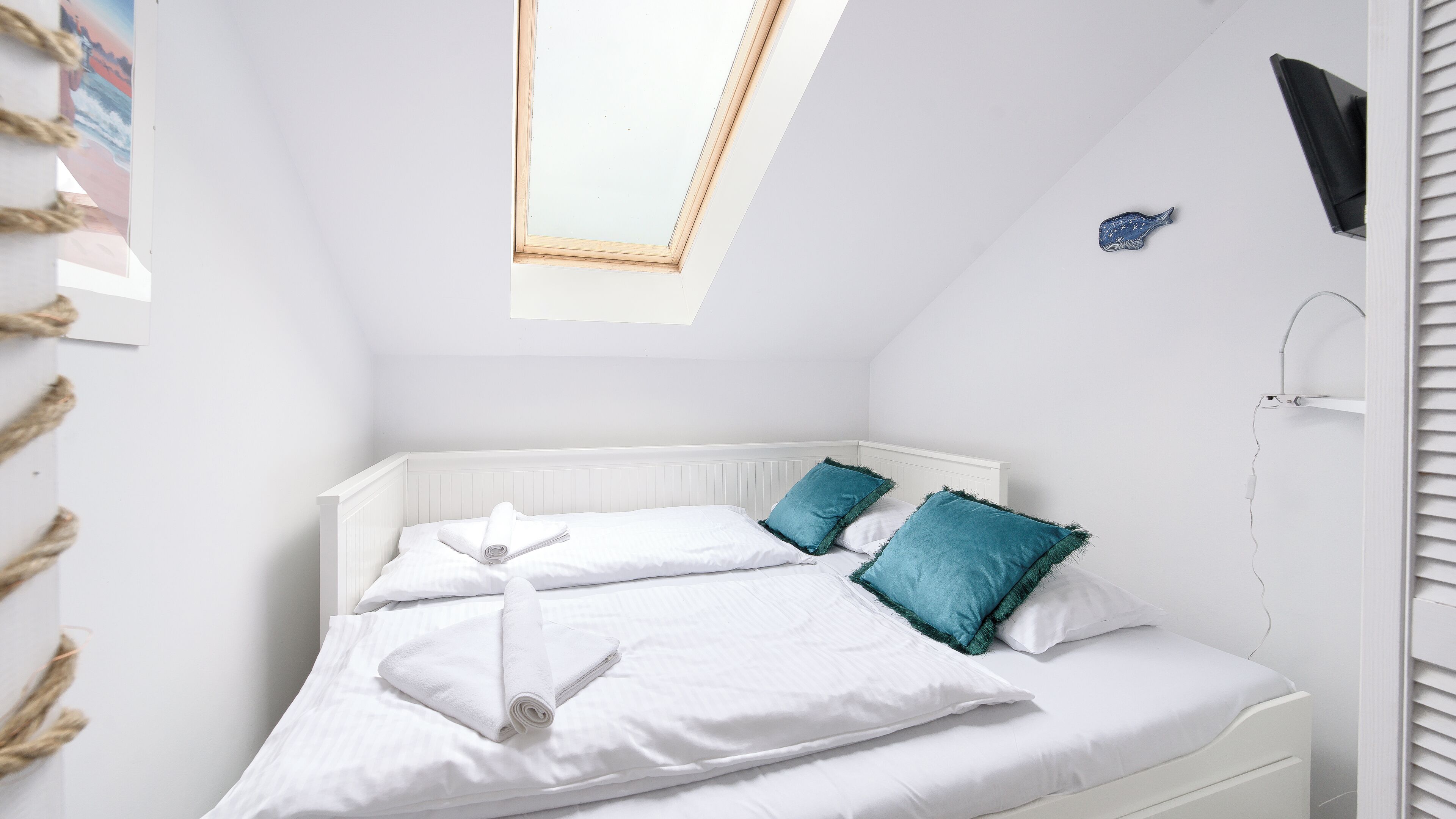 A bedroom with a skylight, white bedding, and teal pillows.