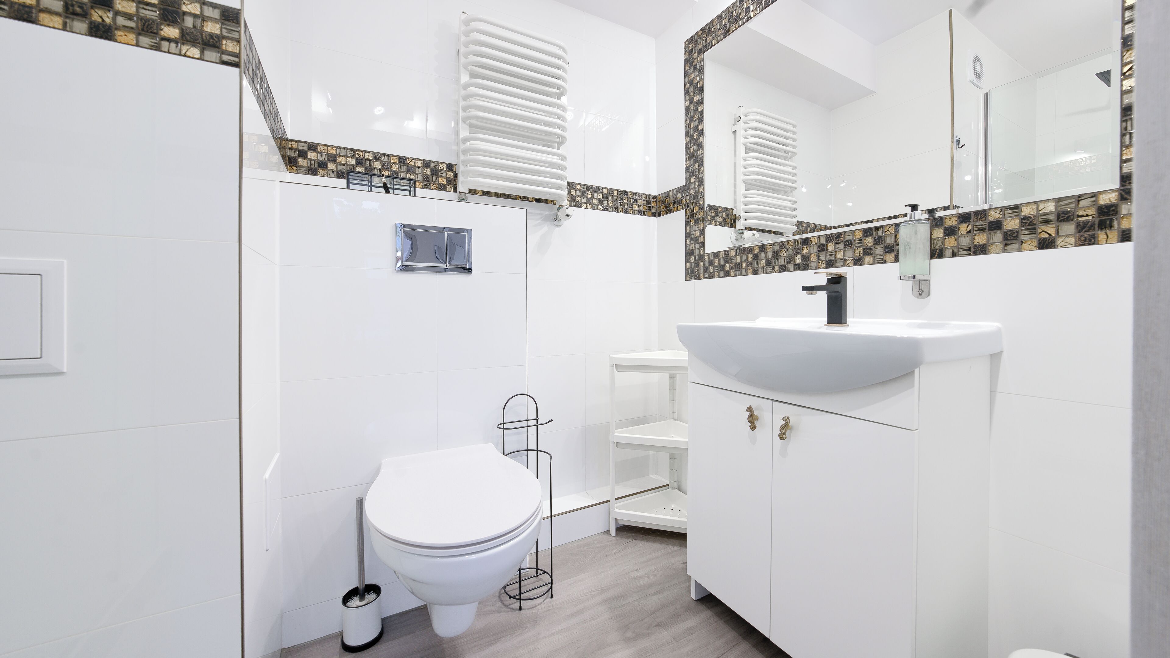 Un baño moderno con inodoro blanco, lavabo con grifo negro y espejo sobre el lavabo.