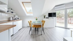 A modern kitchen with a dining area, featuring a skylight, white cabinetry, and a flat-screen TV. - Apartamenty Sun & Snow Grunwaldzka (Pobierowo)