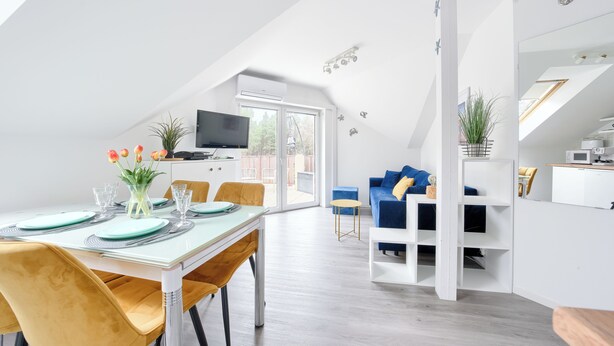 A modern, open-plan living space with a dining area, a blue sofa, and a kitchen area. - Apartamenty Sun & Snow Grunwaldzka (Pobierowo)
