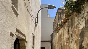 A narrow alleyway with a building on the left and a wall on the right. There is a street lamp and a door on the left side. - Cozy two-room apartment in the heart of Netino Baroque (Noto)