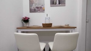 A dining area with a wooden table, two white chairs, and two wall-mounted pictures. - Cozy two-room apartment in the heart of Netino Baroque (Noto)