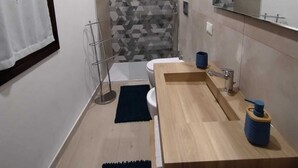 A modern bathroom with a wooden vanity, a mirror, a toilet, and a shower area. - Cozy two-room apartment in the heart of Netino Baroque (Noto)