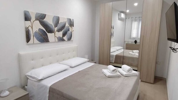 A modern bedroom with a bed, a nightstand, a mirror, and a wall-mounted artwork. - Cozy two-room apartment in the heart of Netino Baroque (Noto)