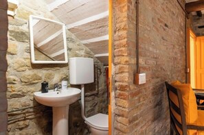 Ein Badezimmer mit Steinwänden, einem Waschbecken, einem Spiegel und einer Toilette.