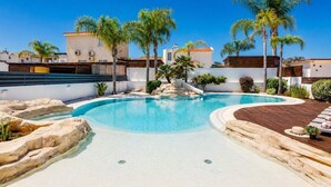 Una piscina de diseño curvo, rodeada de palmeras y un muro blanco.