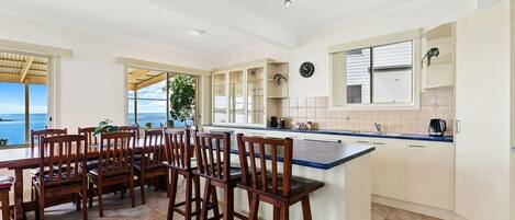 A spacious kitchen with a large island, wooden chairs, and a view of the ocean.