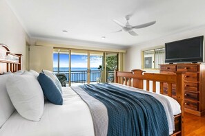 Quarto com cama, televisão, ventoinha no teto e varanda com vista para o oceano.