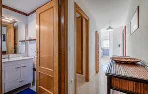 Un pasillo con puertas de madera, un baño con lavabo y espejo, y un comedor con mesa y sillas.