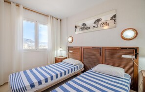 Habitación de hotel con dos camas, una ventana con cortinas, una mesita de noche con lámpara, un espejo en la pared y un cuadro de animales.