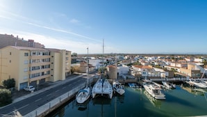 A marina with boats docked, a road adjacent to the water, and residential buildings in the background. - Agi Cap Trencat 146 Apartamento for rent in Roses Girona. (Roses)