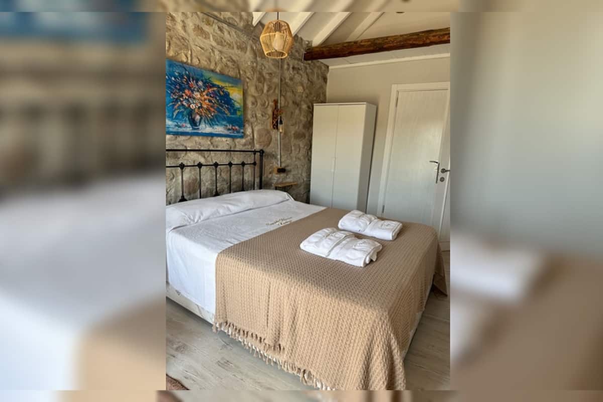 A bedroom with a stone wall, a bed with white linens, a painting, and a door.