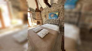 A bedroom with a stone wall, a bed with white linens, and a painting above the bed.