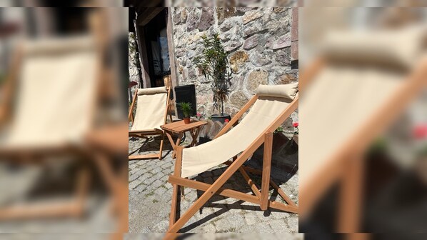 Two wooden lounge chairs with beige cushions, a stone wall, and a potted plant.