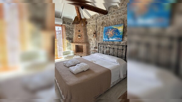 A bedroom with a stone wall, a bed with white linens, and a painting above the bed.