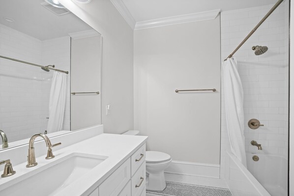 Un baño moderno con un lavabo, tocador y váter blancos. Incluye una zona de ducha con puerta de vidrio y una bañera.