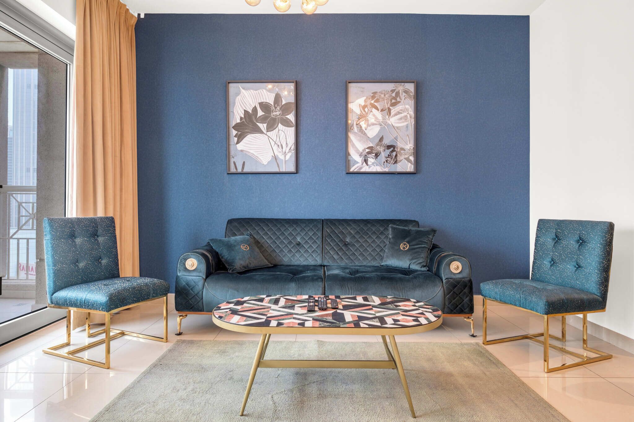 Ein modernes Wohnzimmer mit blauer Wand, zwei gerahmten floralen Kunstwerken, einem dunkelblauen Sofa und zwei passenden Sesseln.