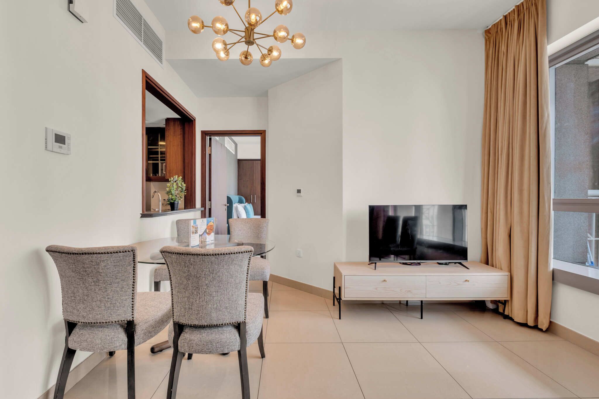 A modern living room with a dining area, a TV, and a large window with curtains.