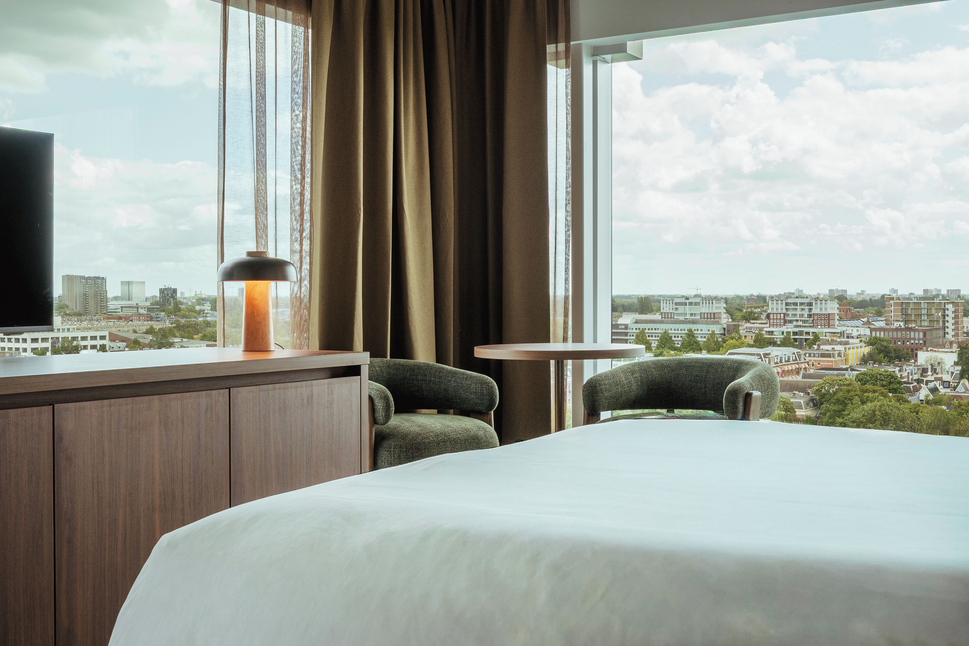 Una habitación de hotel con una cama, dos sillas, una mesita, una lámpara y un televisor.