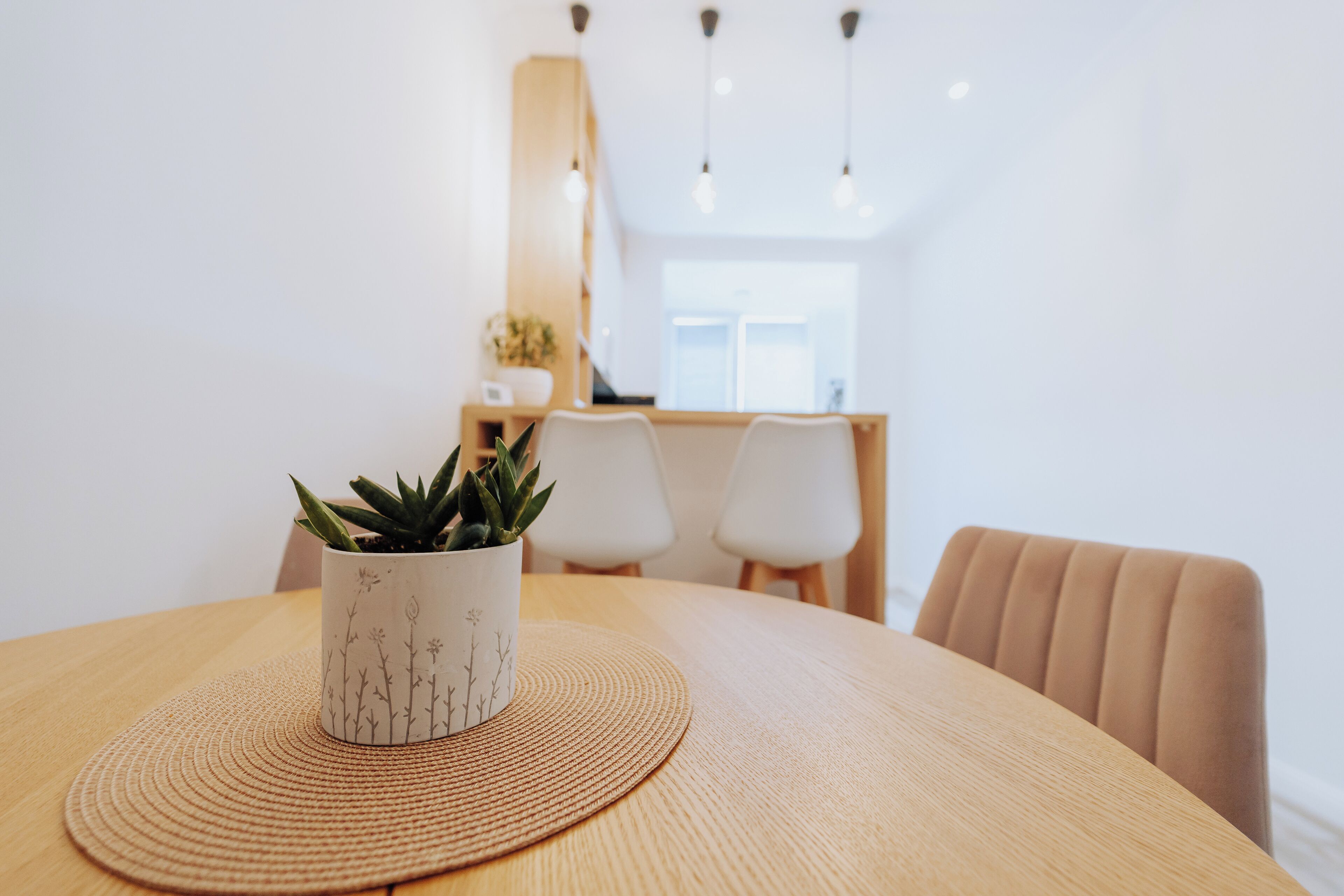 A round wooden table with a woven placemat, a potted plant, and a chair.