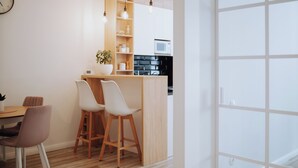 A modern kitchen with wooden cabinets, a microwave, and a dining area with two white chairs and a wooden table.