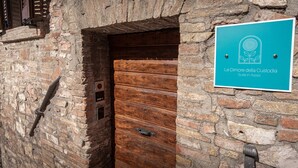 Een rustieke bakstenen muur met een houten deur en een bordje met de tekst 'Le Dimore della Custodia Suite in Assisi'.